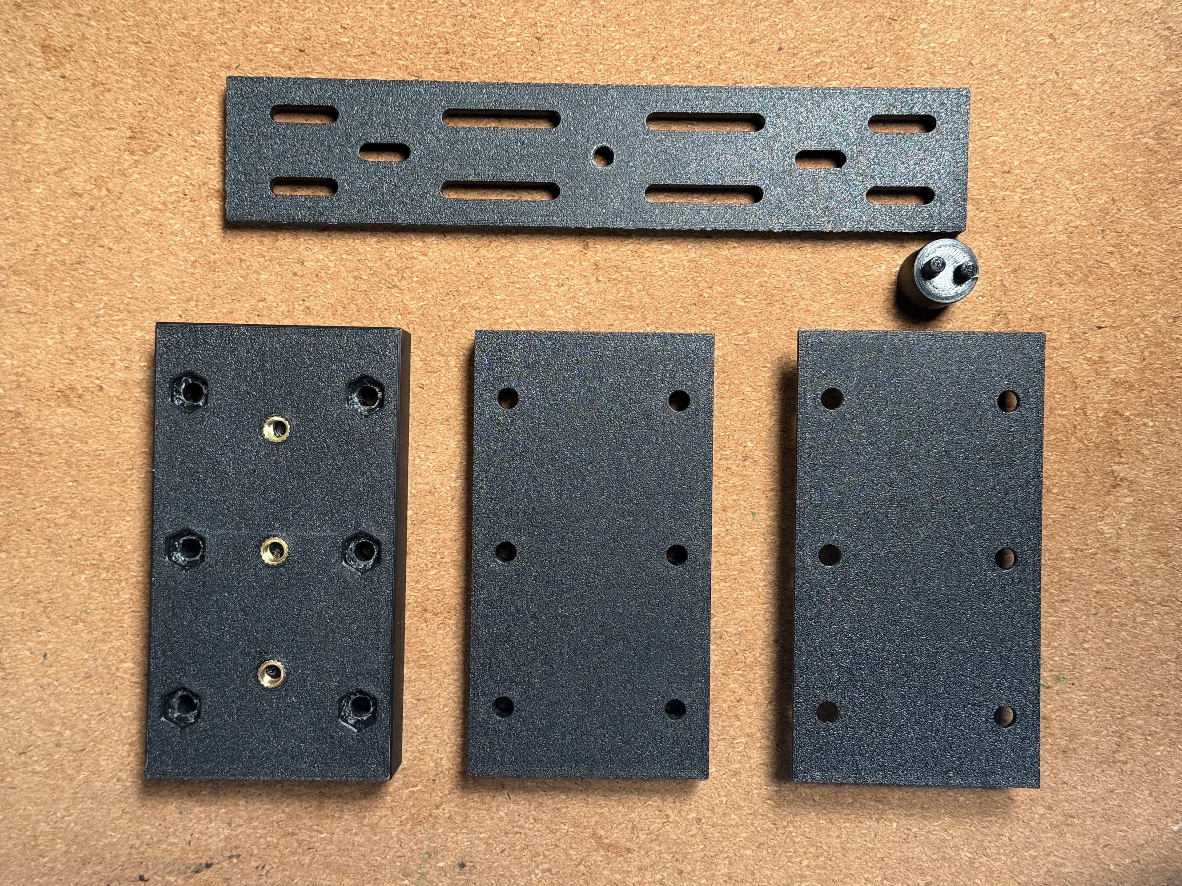 Set of black 3D printed brackets and hardware on a brown cardboard background